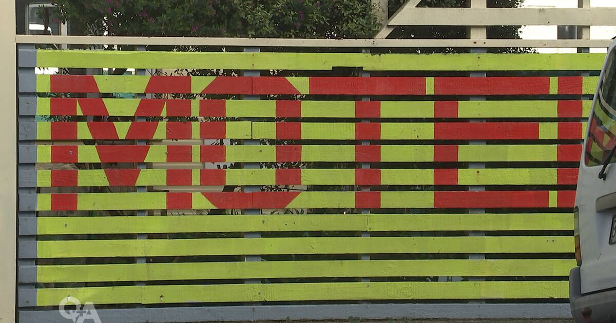 A roadside fence painted with the word MOTEL in bright red letters on a yellow background, illustrating concerns about emergency housing motel grants.