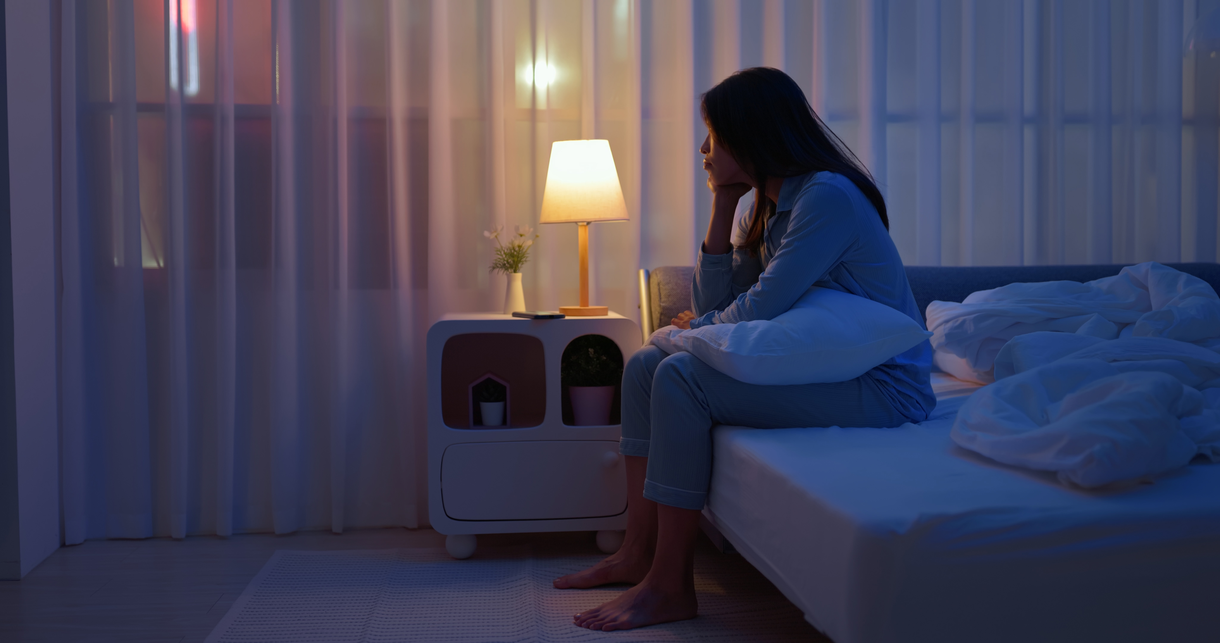 A woman sitting awake on the edge of a bed in a darkened room.