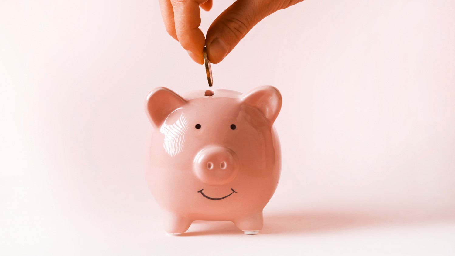 A coin being placed in a piggybank, illustrating KiwiSaver policy coverage.